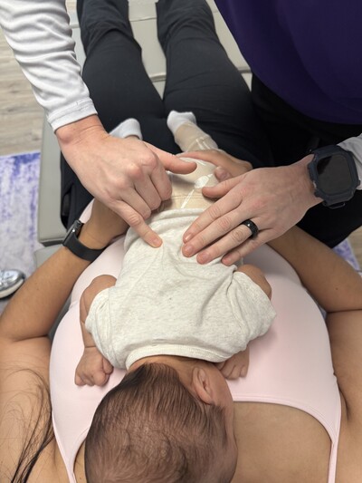 Dr. Hughes adjusting a pediatric patient while the baby is lying on the mom's stomach for comfort. 