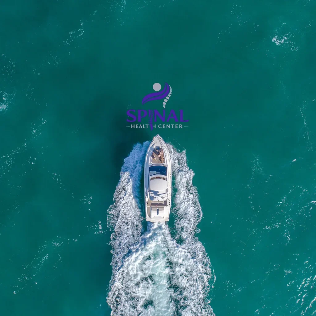 Aerial view of a white boat cruising across turquoise water with the Spinal Health Center logo