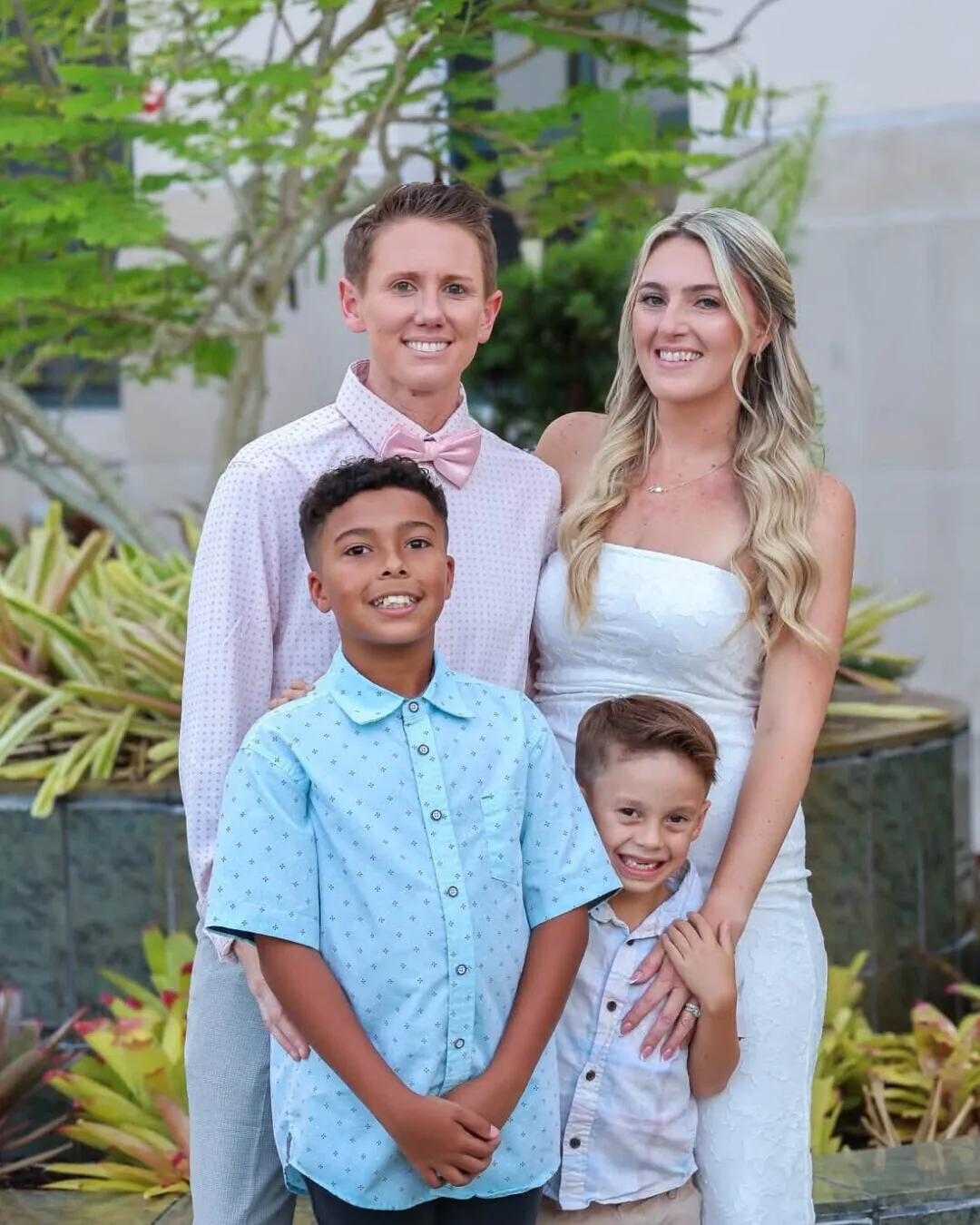 Family of four, two adults and two boys, posing together among tropical plants