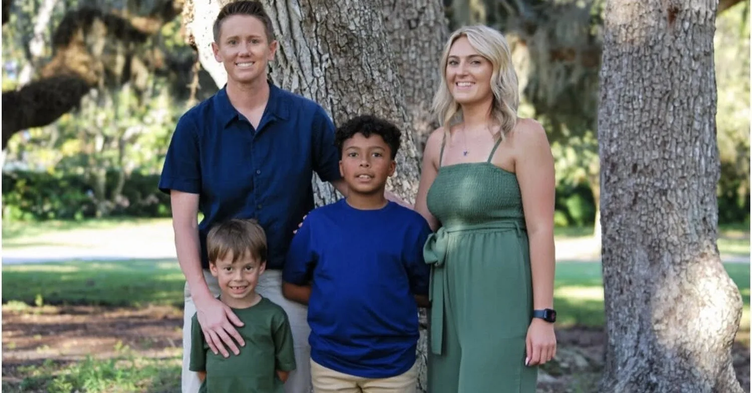Family of four posing together under large oak trees