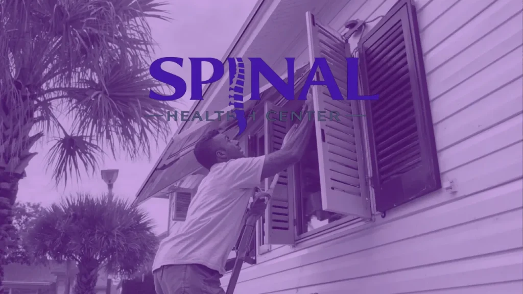 Man on a ladder closing hurricane shutters on a house, with the Spinal Health Center logo